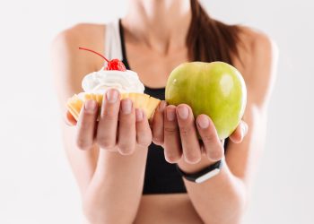 Close up portrait of a sportswoman holding cupcake and an apple isolated over white background