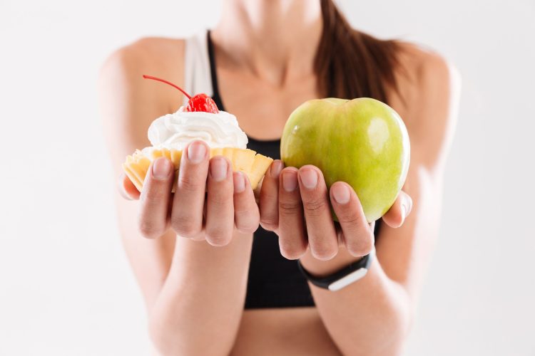 Close up portrait of a sportswoman holding cupcake and an apple isolated over white background