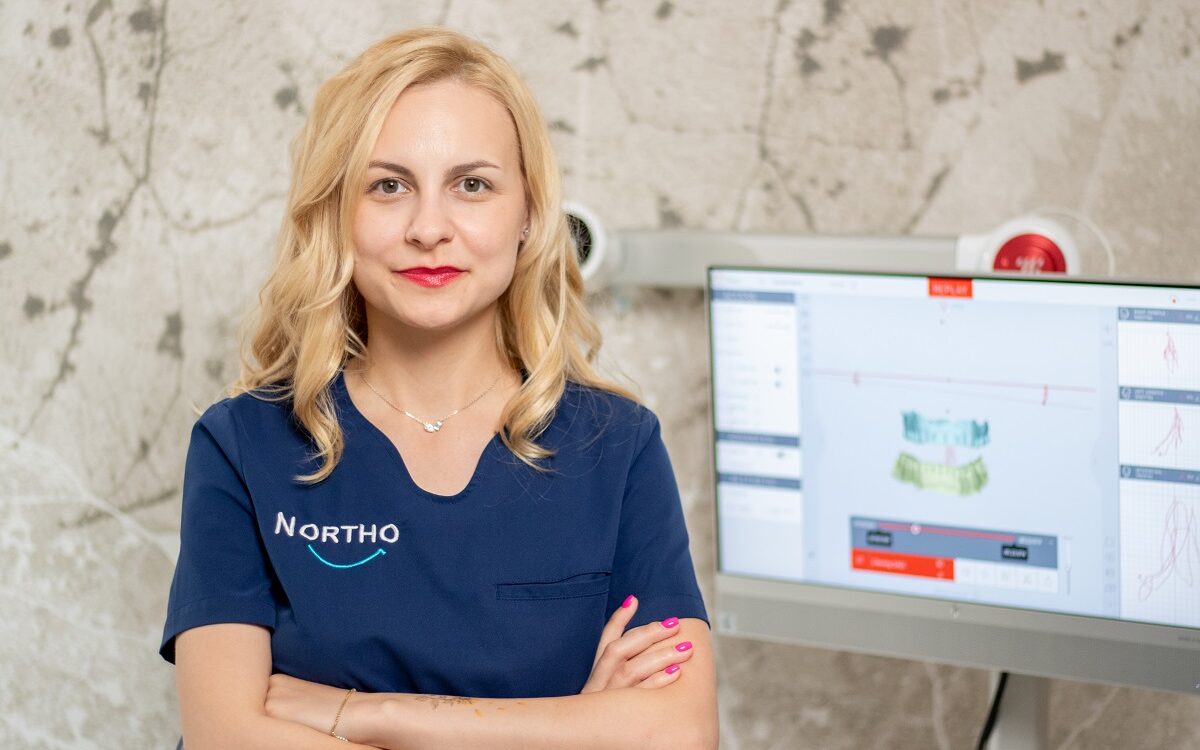 Medic ortodont în clinică, lângă monitor dentar